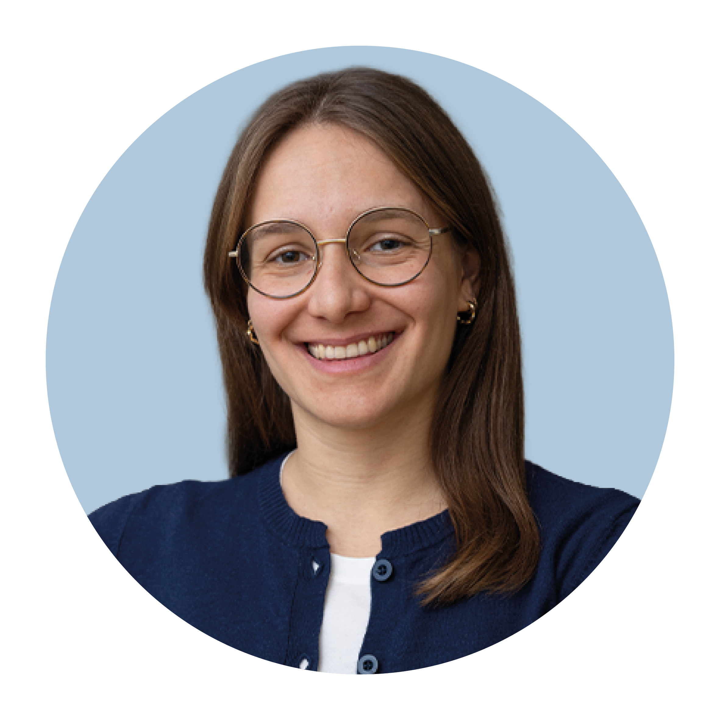 Portrait of Dominique Eggenberger, a white woman with mid-length, brown hair worn loose, wearing a blue top, glasses, and smiling.