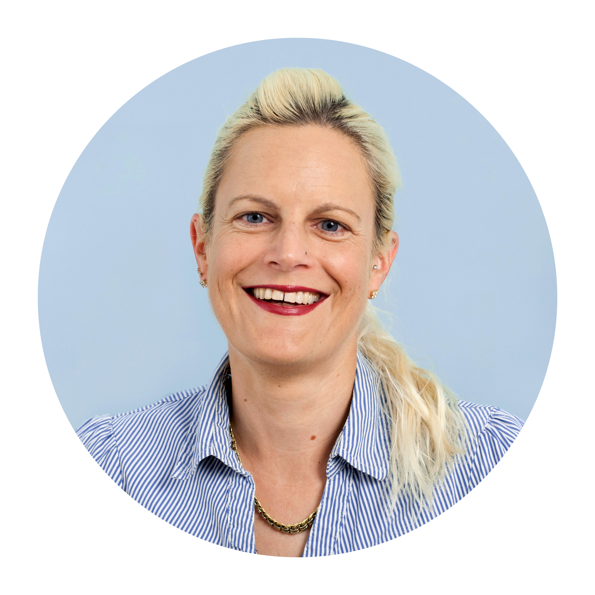Portrait of Nicole Borel, a white woman with medium-length blonde hair tied back, wearing a light blue top and smiling broadly.